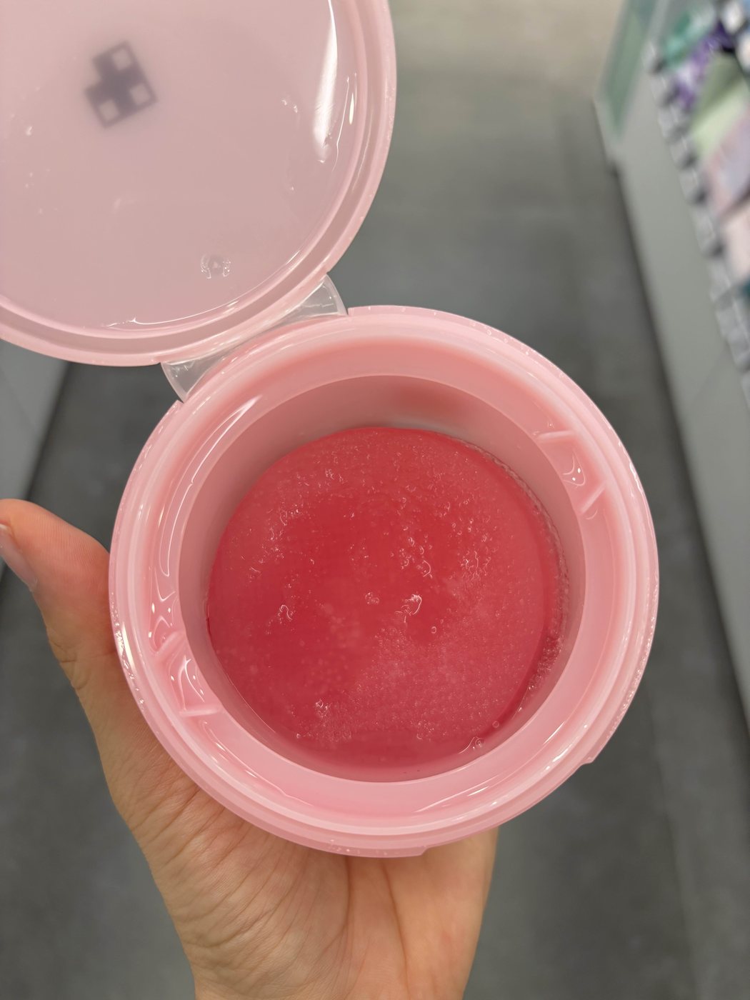 An opened Medicube PDRN toner pad jar held in a store aisle, showing the pink gel inside