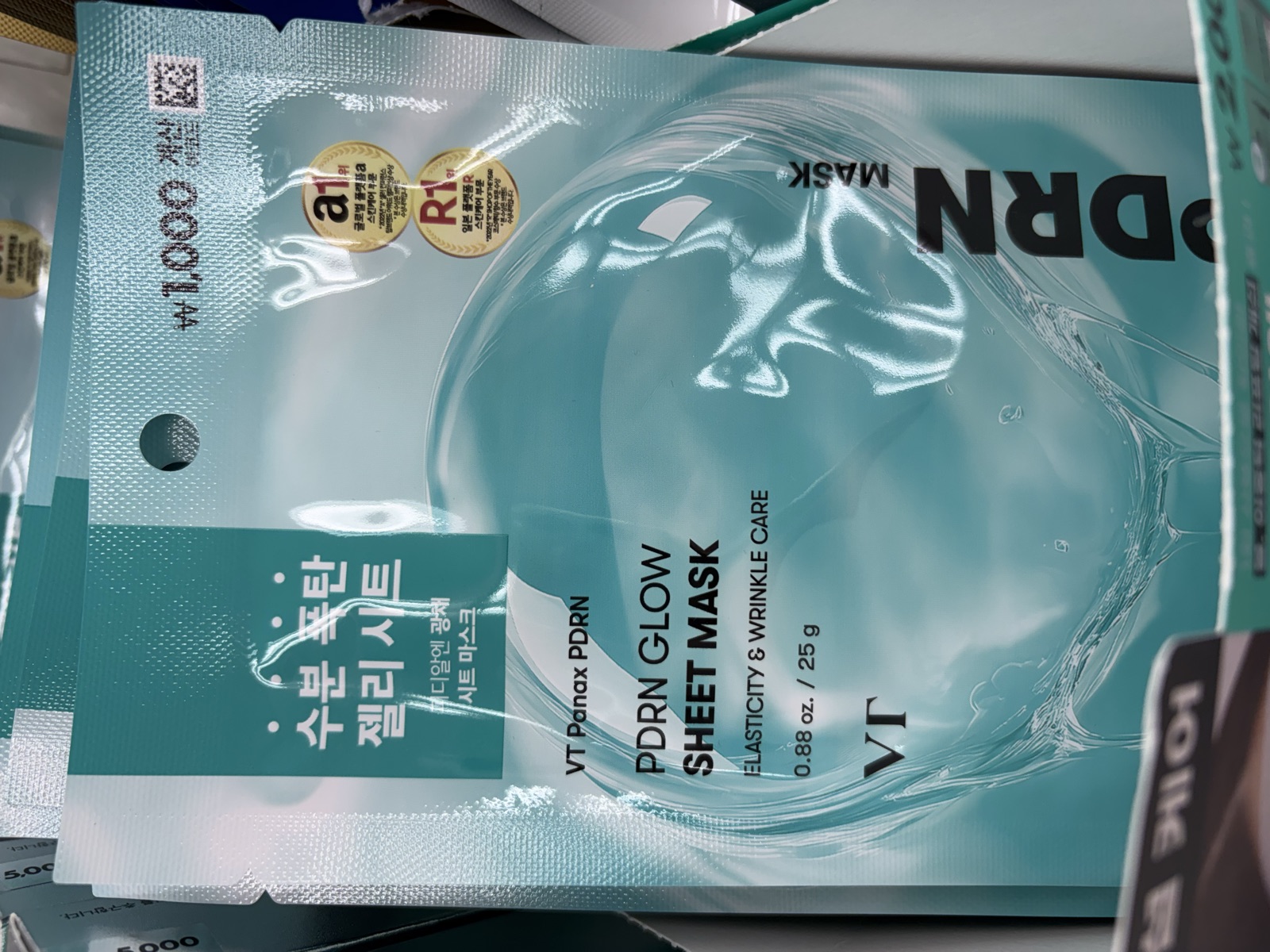 VT Panax PDRN Glow Sheet Mask in teal foil packaging on a Daiso shelf priced at 1,000 won, labeled Elasticity and Wrinkle Care, 25 grams