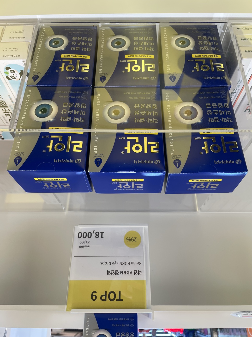 Re-an PDRN eye drops by PharmaResearch displayed under a TOP 9 ranking sign in a Korean pharmacy, blue and gold boxes labeled polydeoxyribonucleotide