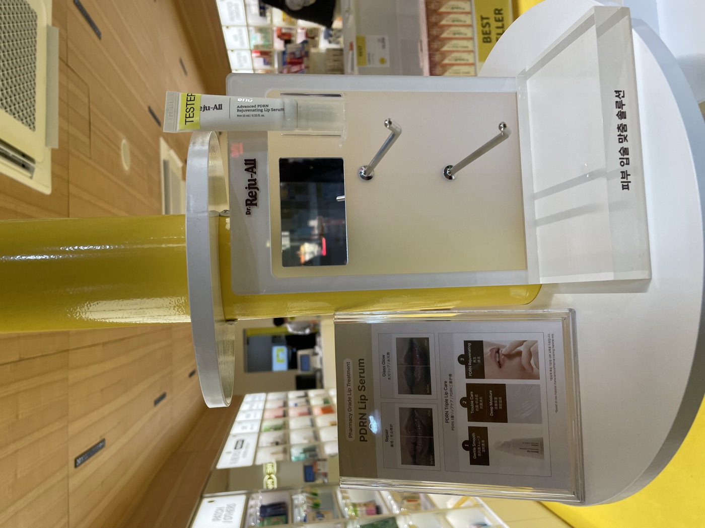 Dr. Reju-All Advanced PDRN Rejuvenating Lip Serum tester on a lit pharmacy display stand with a card describing pharmacy-grade triple lip care