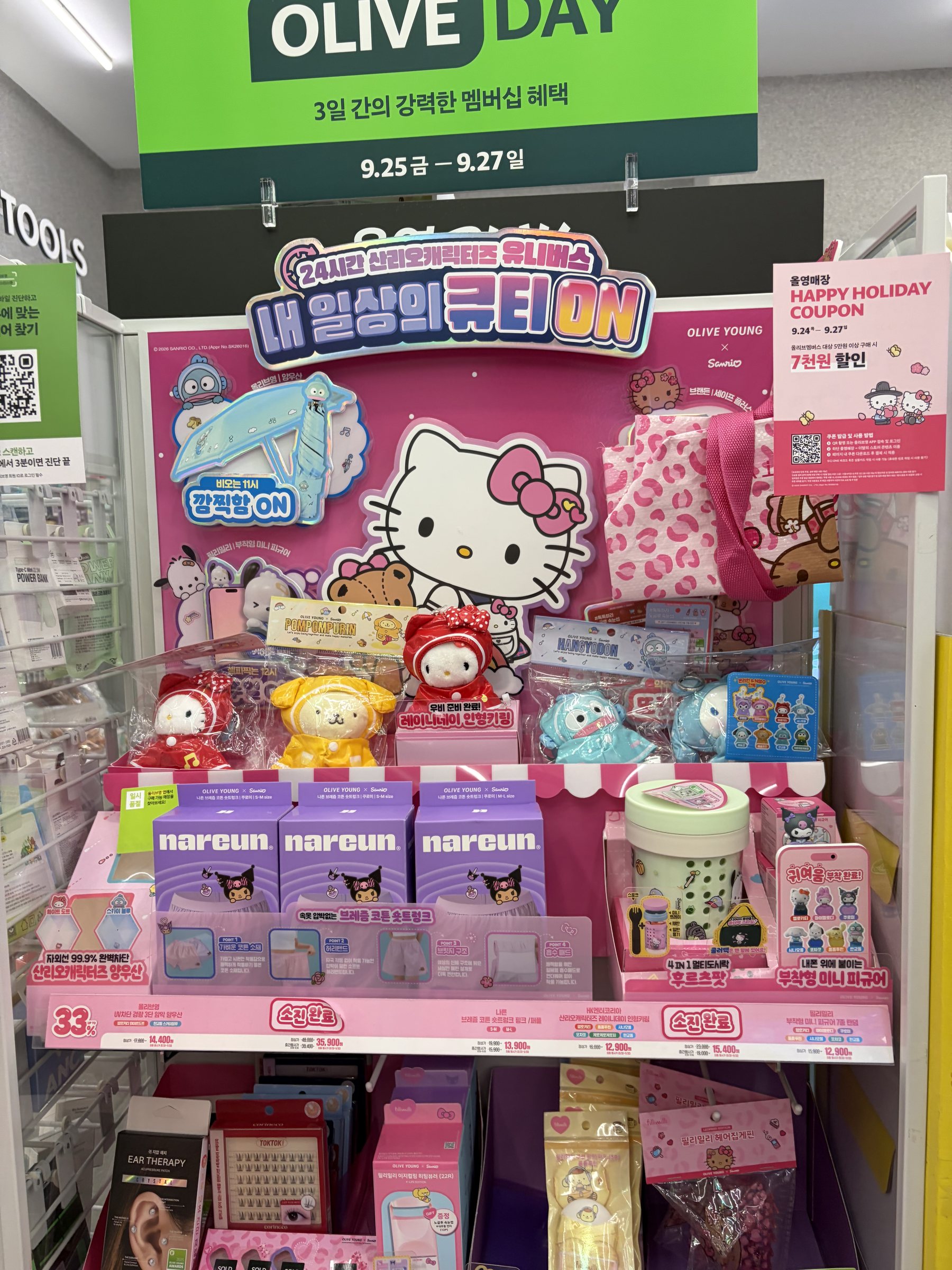 Pink Cutie ON Sanrio merch stand at Olive Young with Hello Kitty display, raincoat plush keyrings and Kuromi Nareun boxes, Olive Day sign above