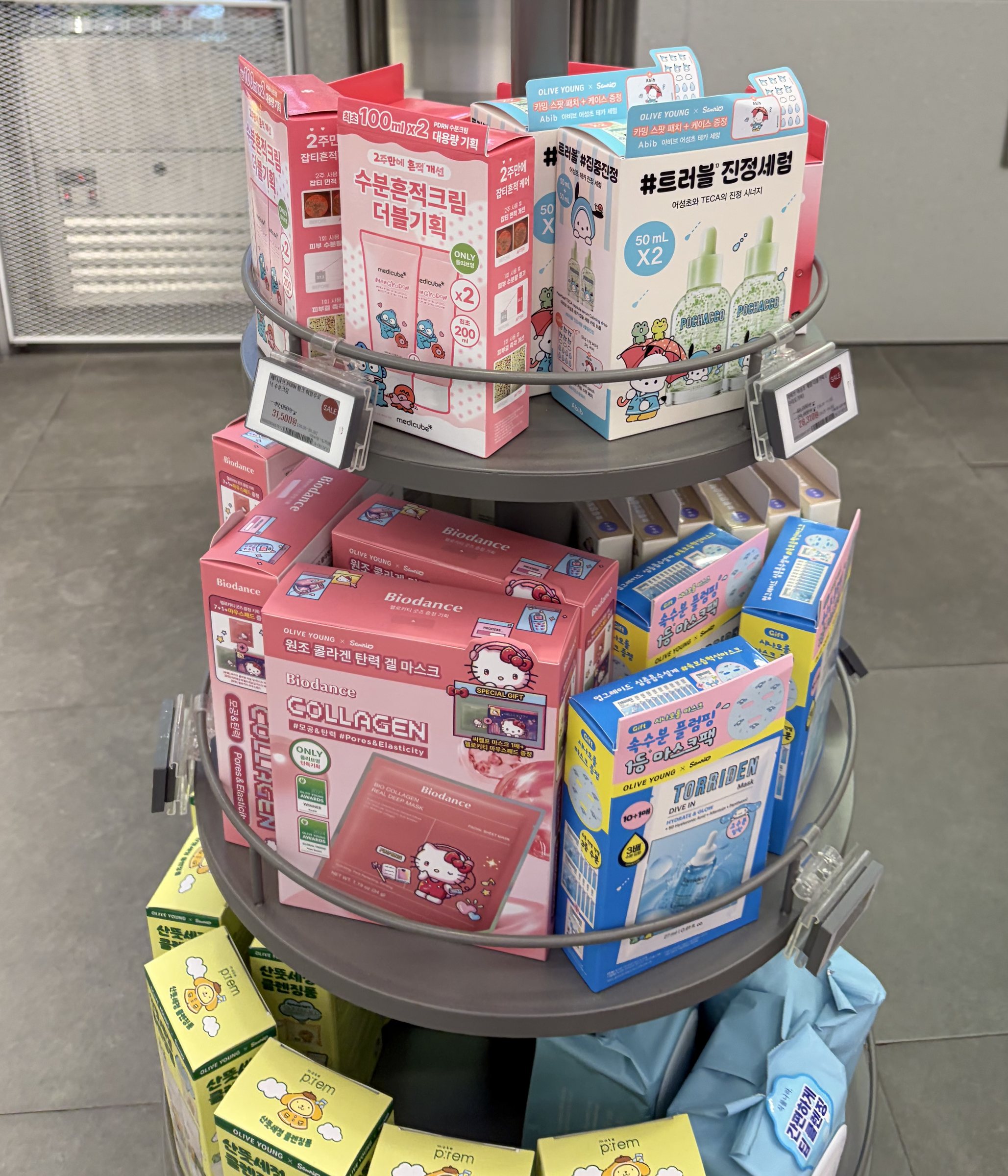 Round Olive Young stand with Medicube Hangyodon PDRN cream double set, Abib Pochacco calming serum, Biodance Hello Kitty collagen masks and Torriden Dive-In masks